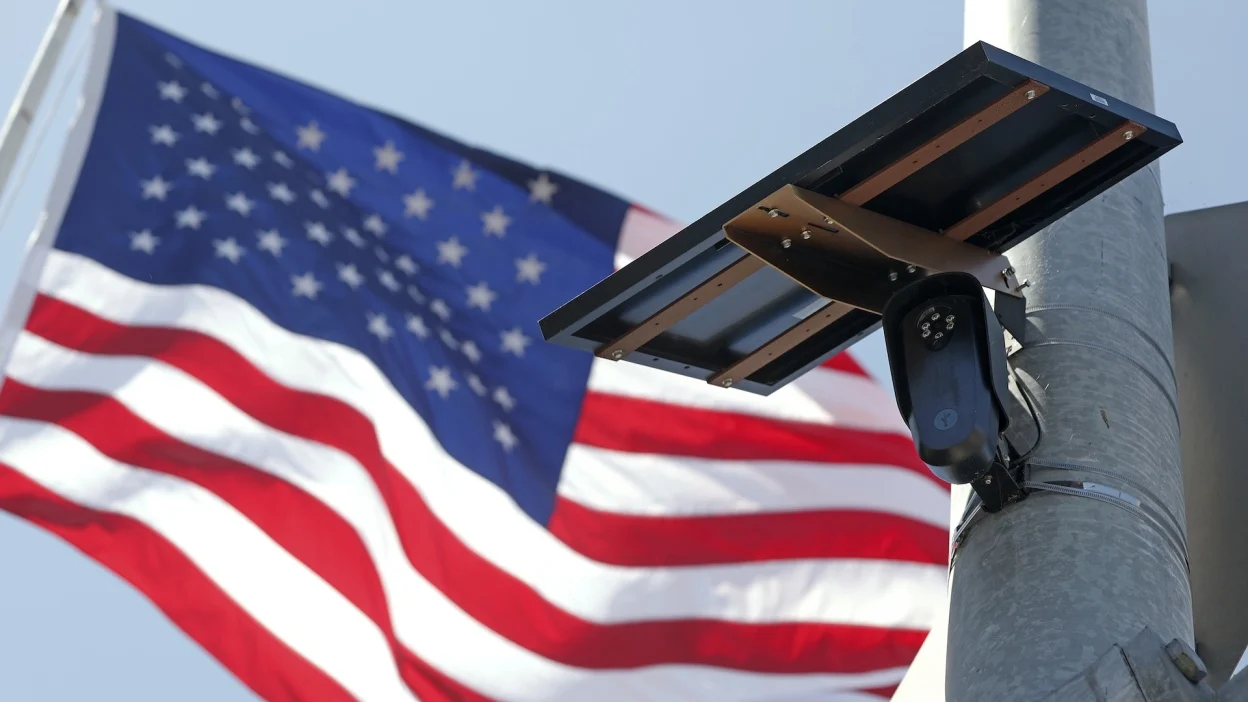 A Flock Safety ALPR camera mounted on a pole in front of an American flag